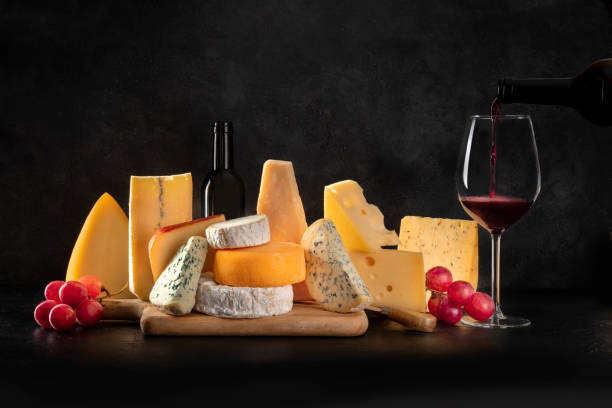 istock Cheese, many different types with grapes and pouring wine, side view on a black background with a place for text 1225789089