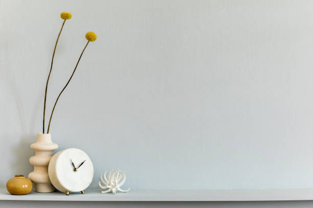 istock Minimalistic composition on the shelf with dried flower in design vase, white clock and accessories. Grey wall. Copy space. 1225794289