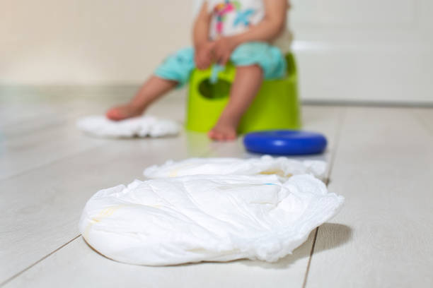 a clean diaper is lying on the bright floor. in the background the child is sitting on a green pot in the blur stock photo
