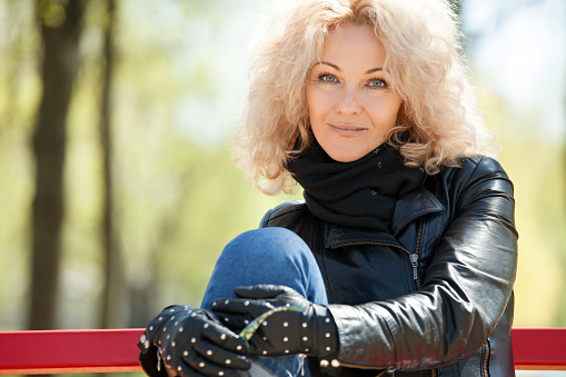 outdoors portrait of a 45 year old blonde woman with curly hair in a black leather jacket