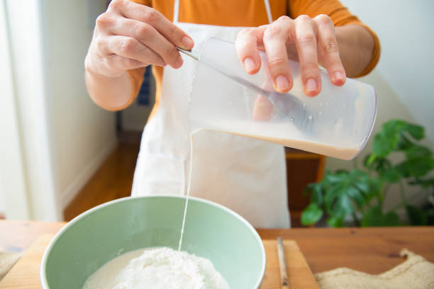 istock Baker in apron adding fresh milk to wheat flour in ceramic bowl 1225796108