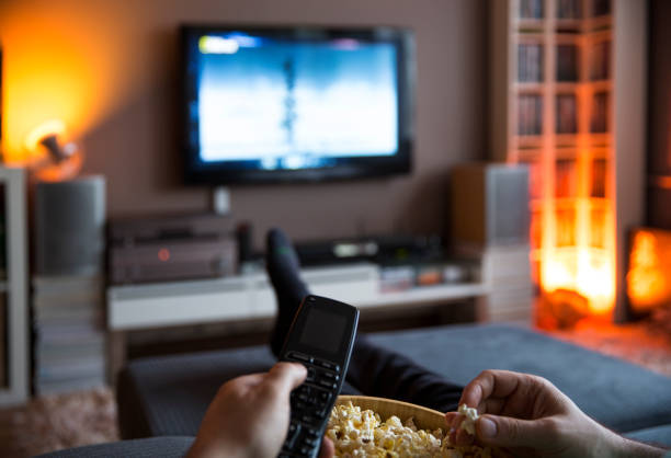 istock Man relaxing at home watching tv and eating popcorn and surfing internet 1225799312