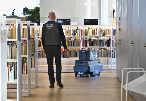 Helsinki, Finland – February 6, 2020: A library employee follows the movement of a transportation robot. Oodi Libray is a popular meeting place in middle of city and has voted for world's best new library in 2019.