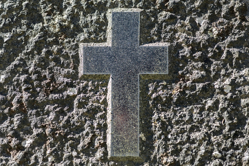 Close up of a smooth cross symbol chiseled on a rough surfaced grave stone