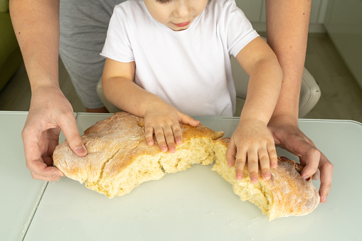 dad and child are breaking freshly baked white bread. family values concept