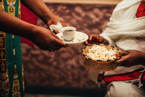 African women's hands holding a cup of coffee and straw bowl with popcorn, a traditional way of preparing coffee in Africa.