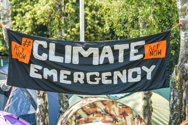 "Climate Emergency" banner hung between trees in a makeshift campsite in Cardiff city centre as part of the climate change protest by Extinction Rebellion. CARDIFF, WALES - JULY 2019: Climate change protesters hung a banner on trees at their makeshift campsite in Cardiff city centre as part of a large demonstration over 3 days extinction rebellion stock pictures, royalty-free photos & images