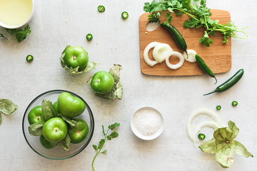 Flat lay of Fresh ingredients to prepare green salsa - Tomatillos, chilies, onion, salt, cilantro