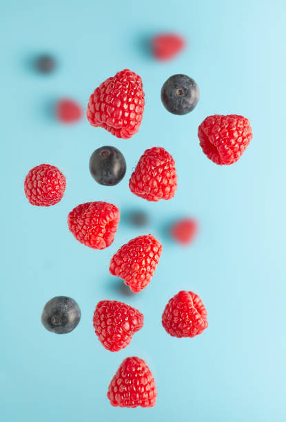 Flying berries over blue table. Falling berries such as raspberry fruits and blueberries