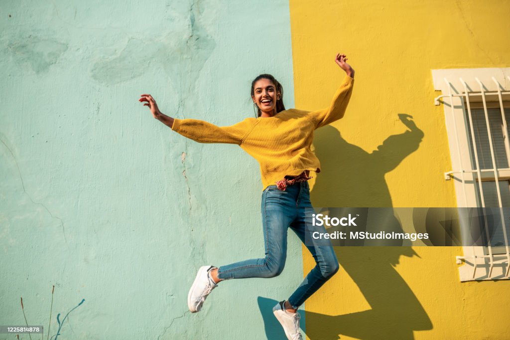 Jump! Young Indian woman jumping.She has light blue wall as a background Women Stock Photo