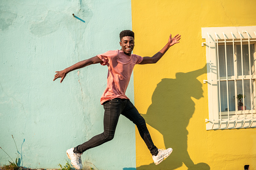 Young man dancing on the street. He has light blue wall as a background