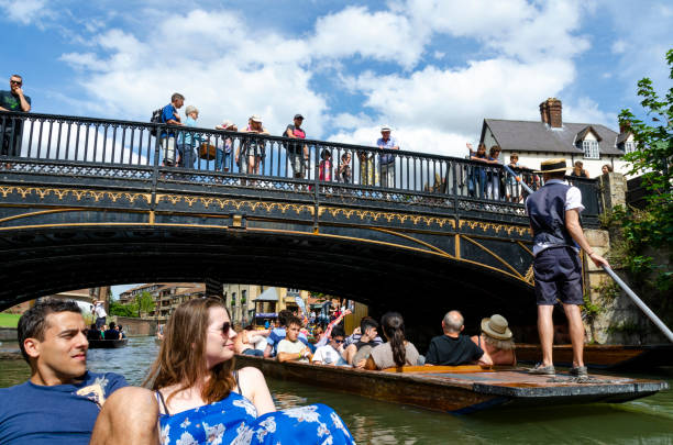 Cambridge, Cambridgeshire, England, The United Kingdom, Great Britain, Europe - March 18, 2024. Punting on the waters of the River Cam in Cambridge.On a winter day in Cambridge, Cambridgeshire, England, a person can be seen punting on the picturesque River Cam. They stand on a traditional flat-bottomed punt boat, using a long pole to propel themselves along the tranquil waters.Captured close to the historic city center, by the iconic architecture of the renowned University of Cambridge colleges. As the person punts leisurely, the warm winter sunlight casts a glow over the scene, reflecting off the water's surface.the quintessential Cambridge experience of punting on the River Cam. This image captures the timeless beauty of this English city, with its rich academic heritage and picturesque waterways.Punting on the River Cam is a tradition in Cambridge, offering a unique vantage point to appreciate the city's architectural marvels and peaceful ambiance. This scene encapsulates the essence of a winter day in the historic heart of Cambridge.