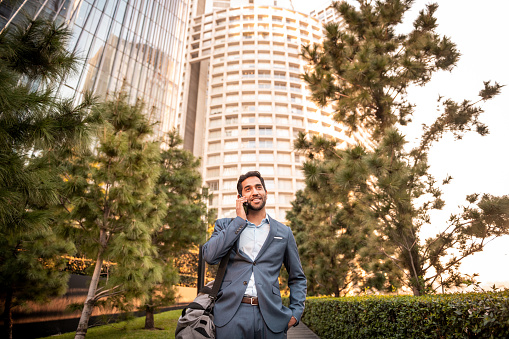 Portrait of a young businessman using a mobile phone. He is walking in front of the office building