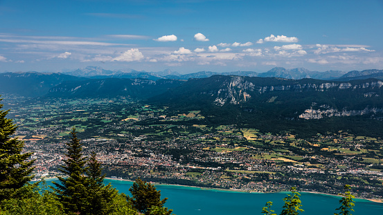 High angle view on Aix les Bains, spa town, on the edge of famous and large Lake Bourget with the European Alps mountains in background. This photo was taken during a sunny summer day from the top of La Dent Du Chat mountain peak in end of Bugey mountains, in border of Ain and Savoie department in Auvergne-Rhone-Alpes region in France, Europe.