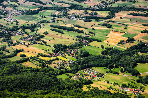 Aerial view of small french village of Lutrin, in middle of rolling landscape. This photo was taken during a sunny summer day at the top of La Dent Du Chat mountain peak in end of Bugey mountains, in border of Ain and Savoie department, in Auvergne-Rhone-Alpes region in France, Europe.