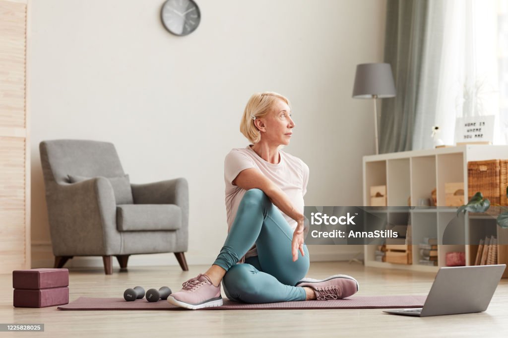 Woman training at home Senior woman sitting on the floor on exercise mat in front of laptop and training at home Exercising Stock Photo