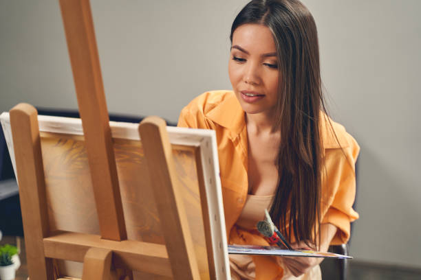 istock Charming young lady painting on easel at home 1225830043
