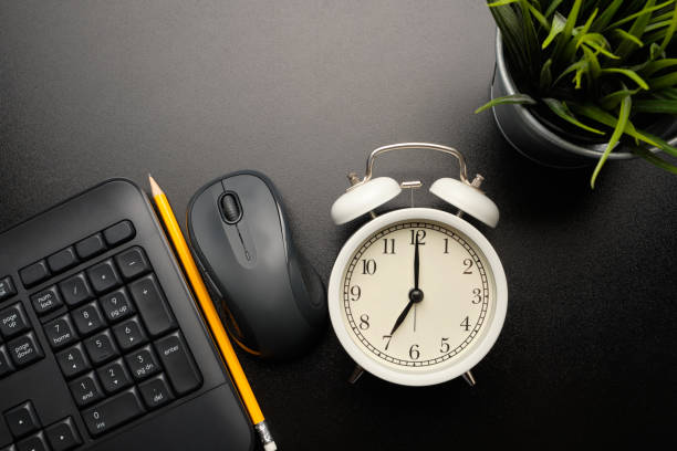 istock Vintage alarm clock in white color on black table that surround with black keyboard, mouse, yellow pencil and tree. 1225834606