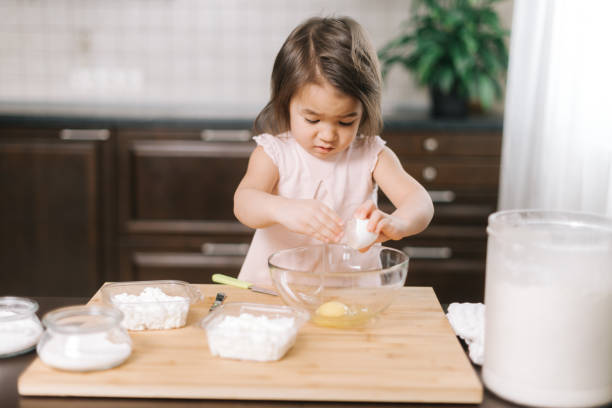 la petite fille mignonne casse un oeuf dans un bol de mélange à la cuisine - break eggs domestic kitchen breaking photos et images de collection