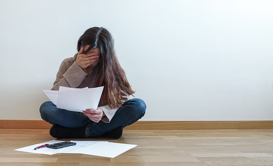 frustrated young woman reviewing documents, covering her face with her hand