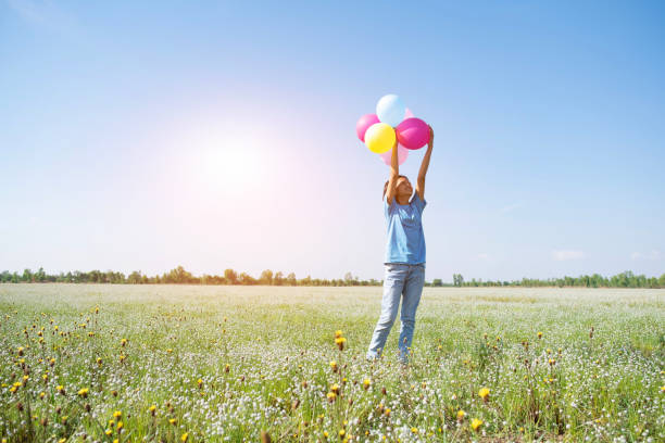 la jeune fille tiennent des ballons colorés à l’herbe de fleur avec le ciel bleu. - sun sky child balloon photos et images de collection