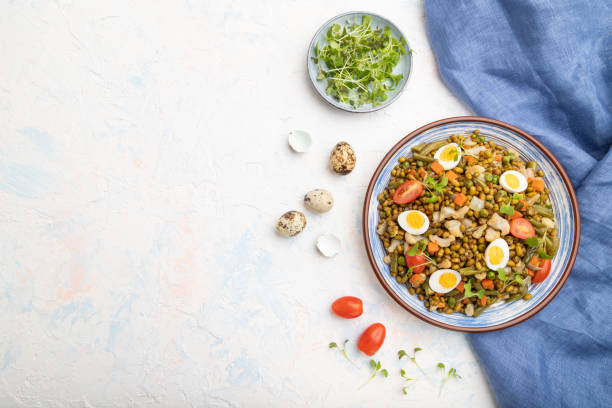Mung bean porridge with quail eggs, tomatoes and microgreen sprouts on a white concrete background and blue textile. Top view, flat lay, copy space.