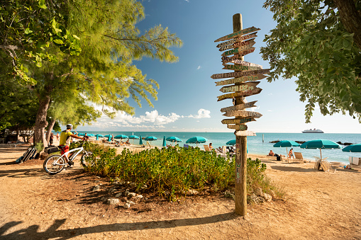 Key West, Florida - December 4, 2019:  People tan and rest by a wooden signpost on the sunny beach of Fort Zachary Taylor State Park in tropical Key West Florida USA