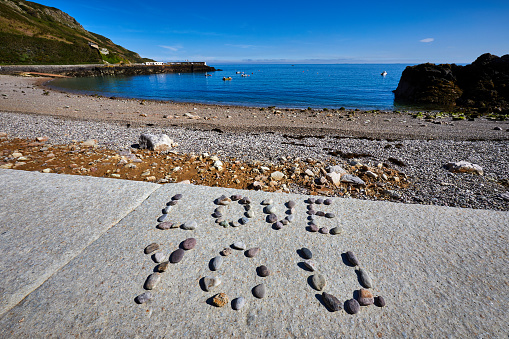 Image of a pebble beach in the early morning sunshine with a small island and harbour in the background with the words LOVE YOU written in pebbles in the forground. Selective Focus
