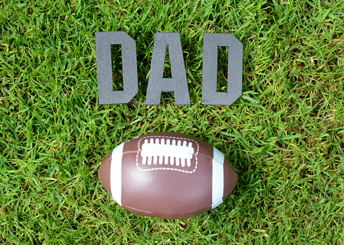 Closeup of generic letter spelling out DAD on a bed of grass with a toy football, symbolizing Father's Day.