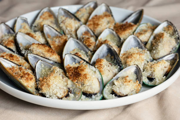 Mussels baked with parmesan, bread crumb and herb butter served on a plate. Food background. Mediterranean cuisine. Concept for a tasty and healthy meal. Close up. stock photo