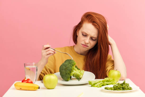 istock Vegetable diet. Sad dull woman holding broccoli on fork while making grimace 1225850775
