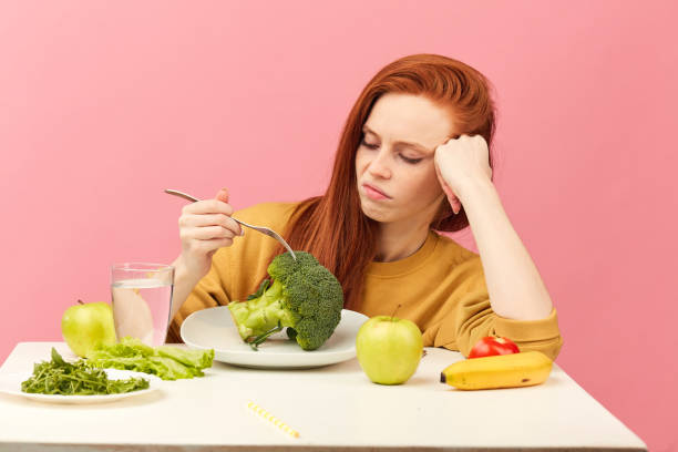 istock Vegetable diet. Sad dull woman holding broccoli on fork while making grimace 1225850780