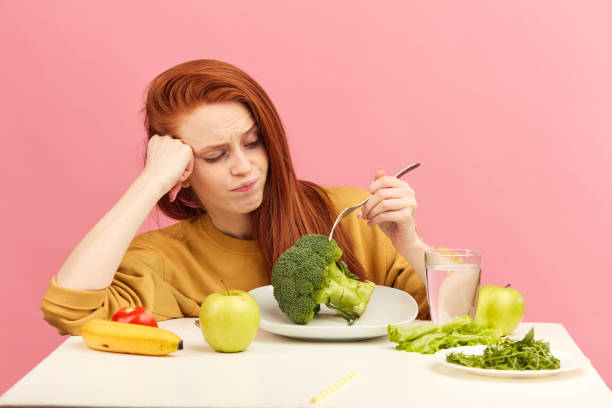 istock Vegetable diet. Sad dull woman holding broccoli on fork while making grimace 1225850939
