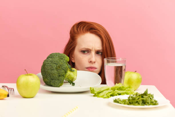 istock Frowning woman dislikes vegetables on table with disgusting grimace isolated 1225850952
