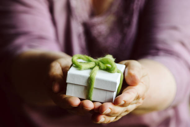 Hands holding a small white gift box  with a self-made green gift ribbon and a flower. shallow depth of field