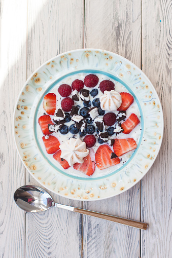 Oatmeal porrige with milk, fresh strawberries, blueberries and raspberries. Top view, wooden background.