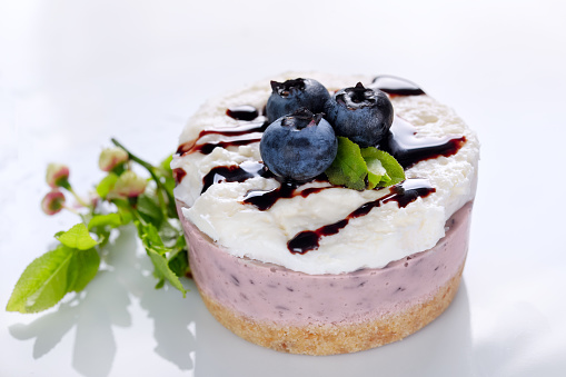 Blueberry yogurt cake decorated with fresh berries and green blueberry sprigs on a white table