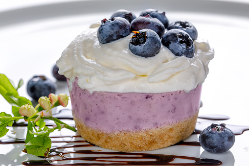 Blueberry yogurt cake decorated with fresh berries and green blueberry sprigs on a white table