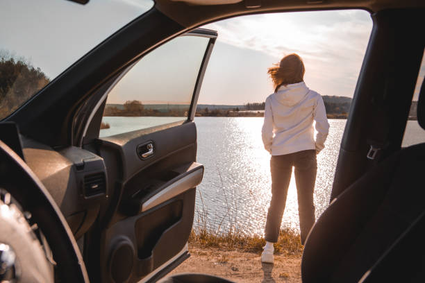 woman stopped car at beach looking on sunset over the water woman stopped car at beach looking on sunset over the water. road trip. car back open stock pictures, royalty-free photos & images