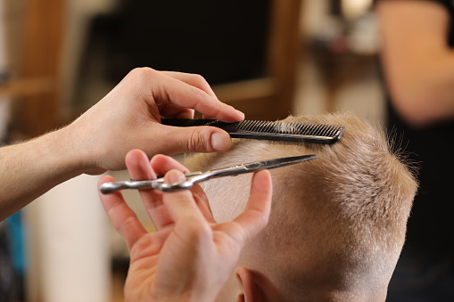 Men's hairstyling, haircutting, in a barber shop or hair salon. Close-up of man hands grooming kid boy hair in barber shop. Portrait of male child at the barber shop to cut his hair