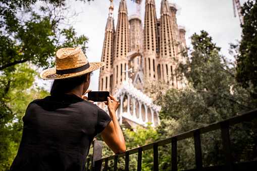 Young Latin woman enjoying the view on Sagrada Familia in Barcelona. She is making a photo with her mobile phone
