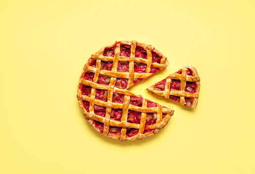 Strawberry-rhubarb pie sliced for one, with a lattice crust, on a yellow seamless background. Flat lay with rhubarb pie. Sweet vegetable tart.