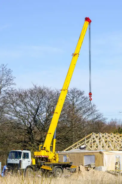 Photo of Truck mounted crane with a telescoping boom at constructing a carcas of a new wooden building