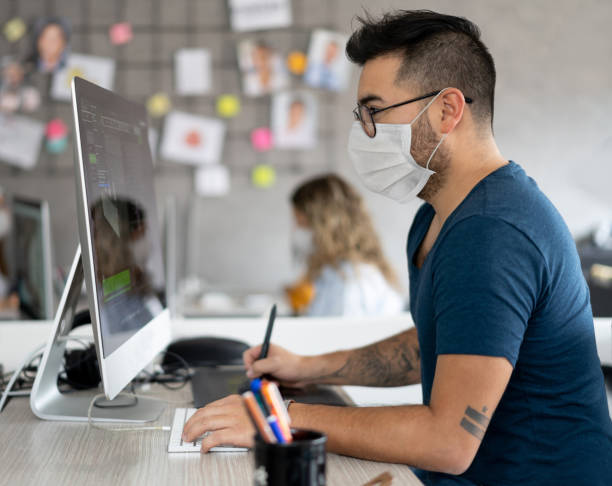 istock Designer working at a creative office wearing a facemask and complying to social distancing 1225861960
