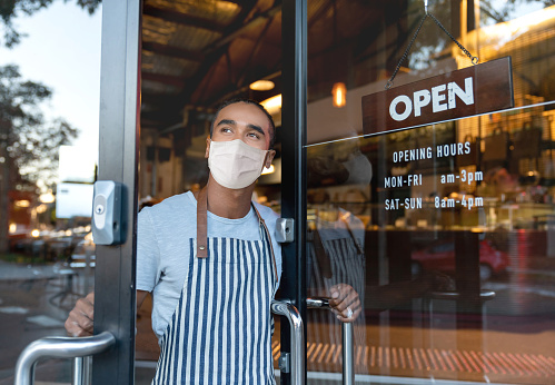 El dueño del negocio abre la puerta en un café con una máscara facial photo