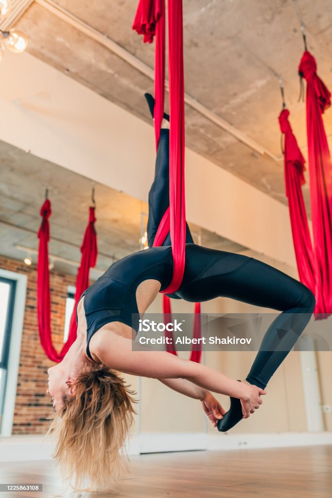 Tânără în salopetă neagră care efectuează exerciții de yoga antigravitațională - Fotografie de stoc Adult fără redevențe Tânără în salopetă neagră care efectuează exerciții de yoga antigravitațională - Fotografie de stoc Adult fără redevențe