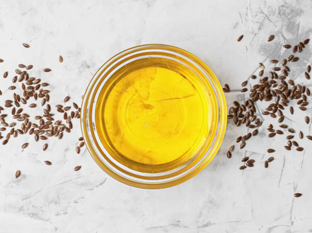 Flaxseed oil in a glass bowl and golden flax seeds on a gray background, top view. Useful natural oil. stock photo