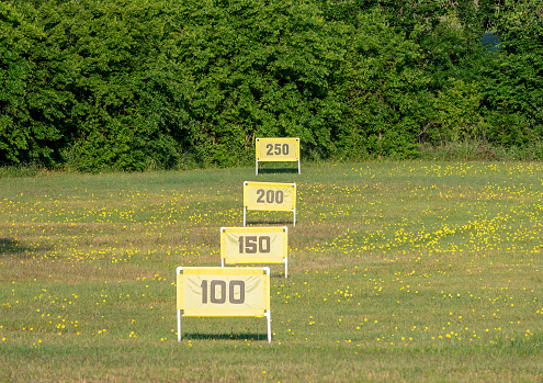 Yellow yardage markers and flowers on a Texas golf driving range with green bushes as a backstop