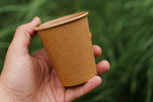 istock Close up isolated eco-friendly natural coffee cup. Disposable ecological utensils in hands on green grass background. Sustainability of planet. Cardboard glass made of fiber of bamboo and bagasse 1225867435