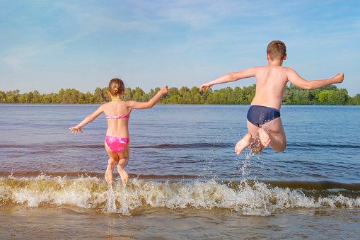 Children jump in the river on the waves on a sunny day. The view from the back.